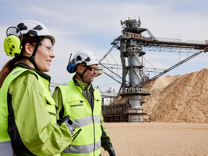 Two employees in safety gear walking by the chip piles at the Äänekoski bioproduct mill area