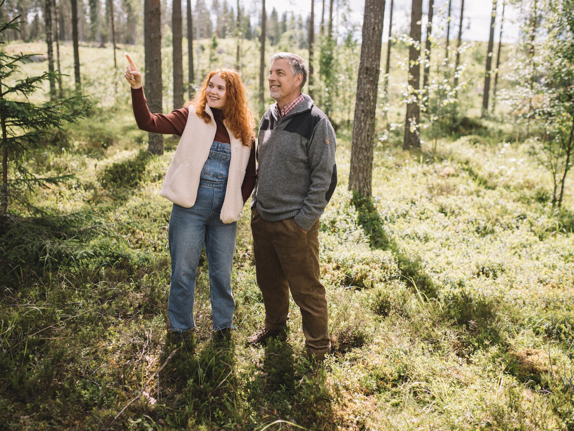 Father and daughter standing in the forest, looking where the daughter is pointing.