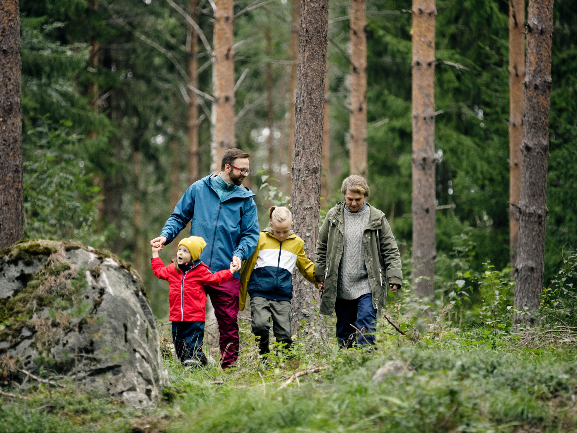 Farmor, far och barn går i skogen mot kameran.