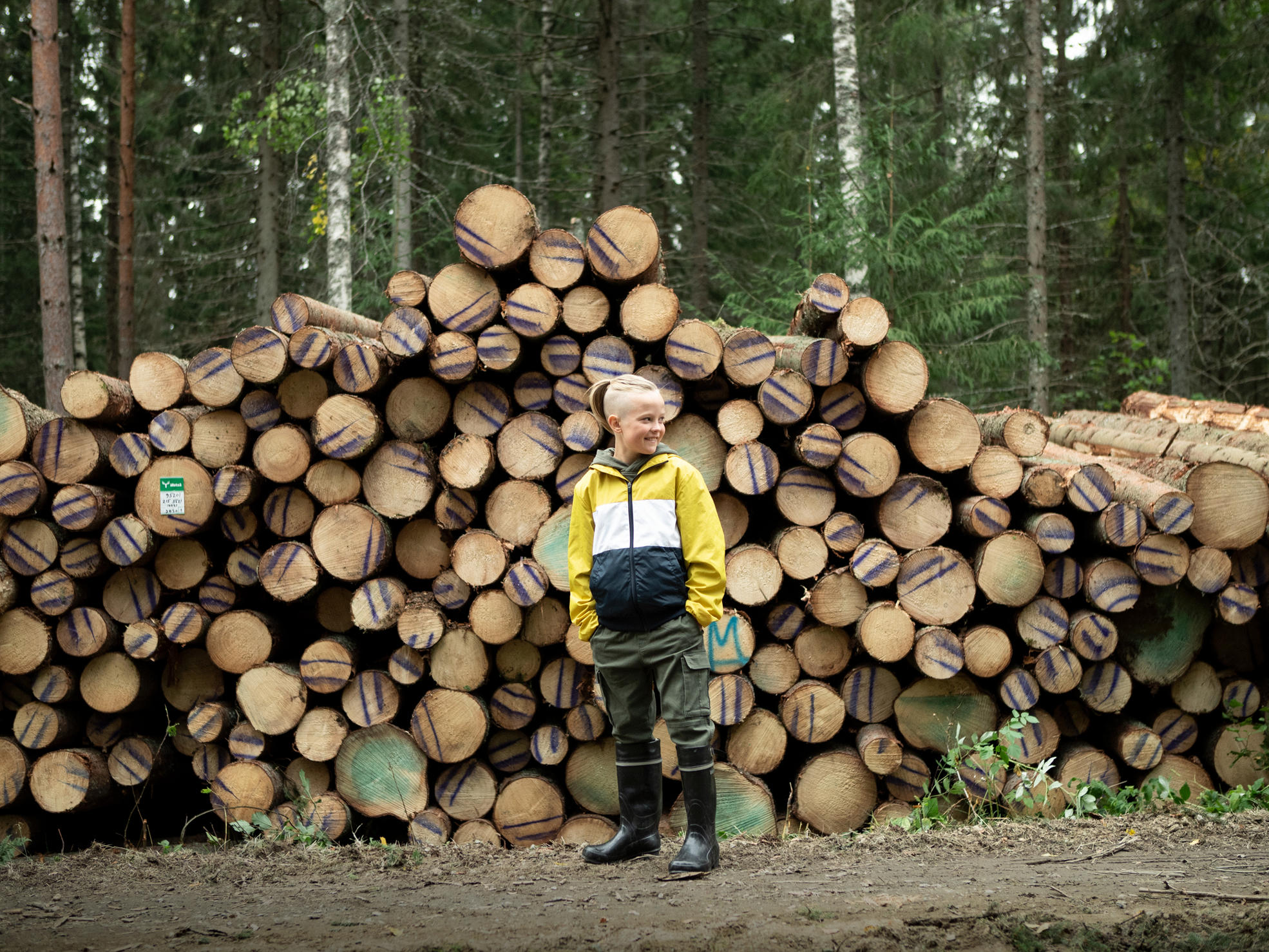 Poika seisoo metsätiellä puupinon edessä.