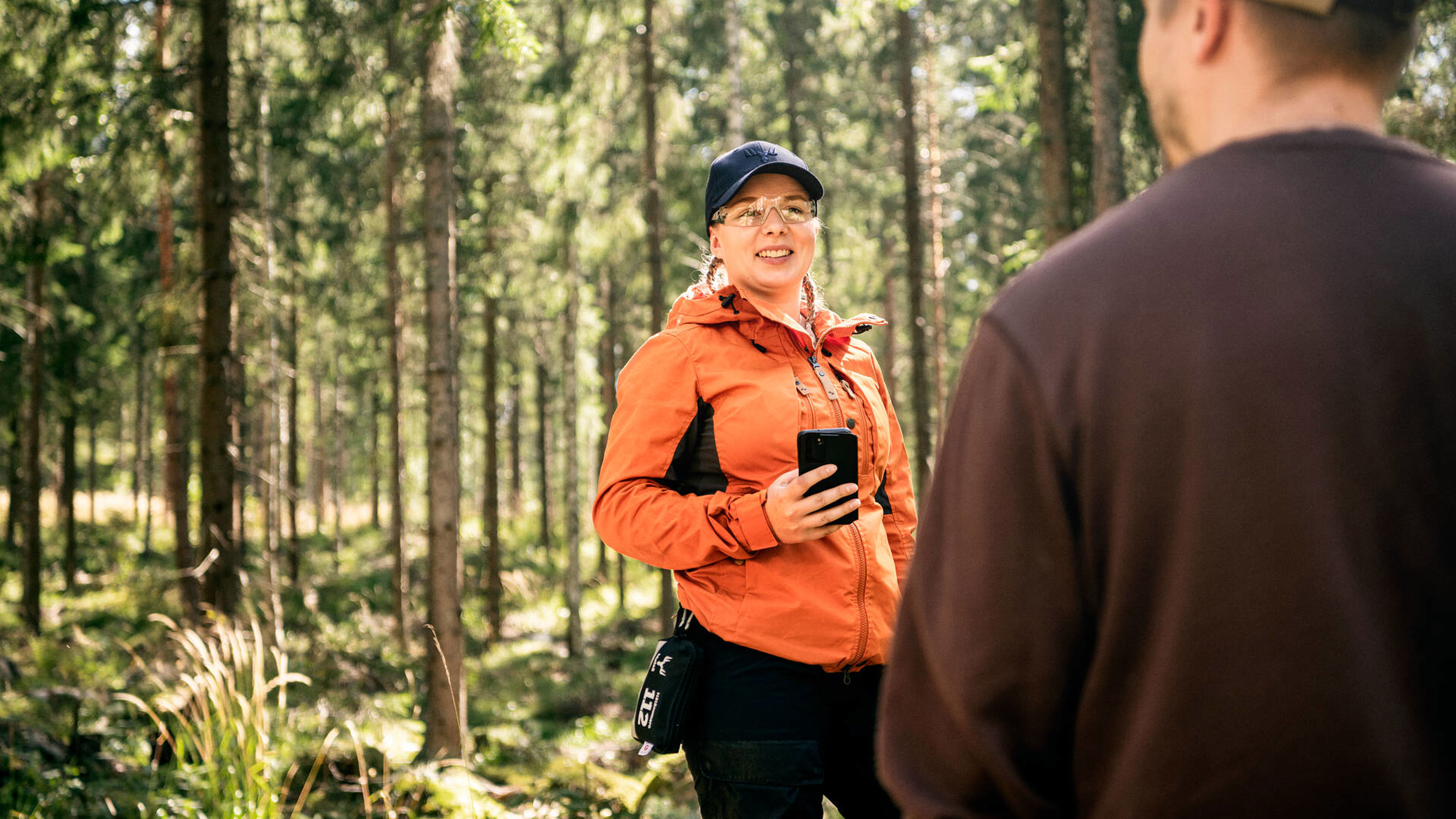 Metsäasiantuntija seisoo metsässä ja juttelee asiakkaalle.